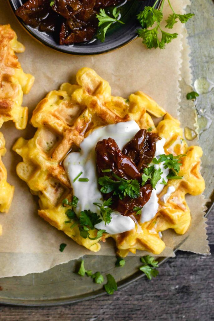 herzhafte kürbiswaffeln mit käse; getoppt mit sauerrahmsauce und eingelegten tomaten