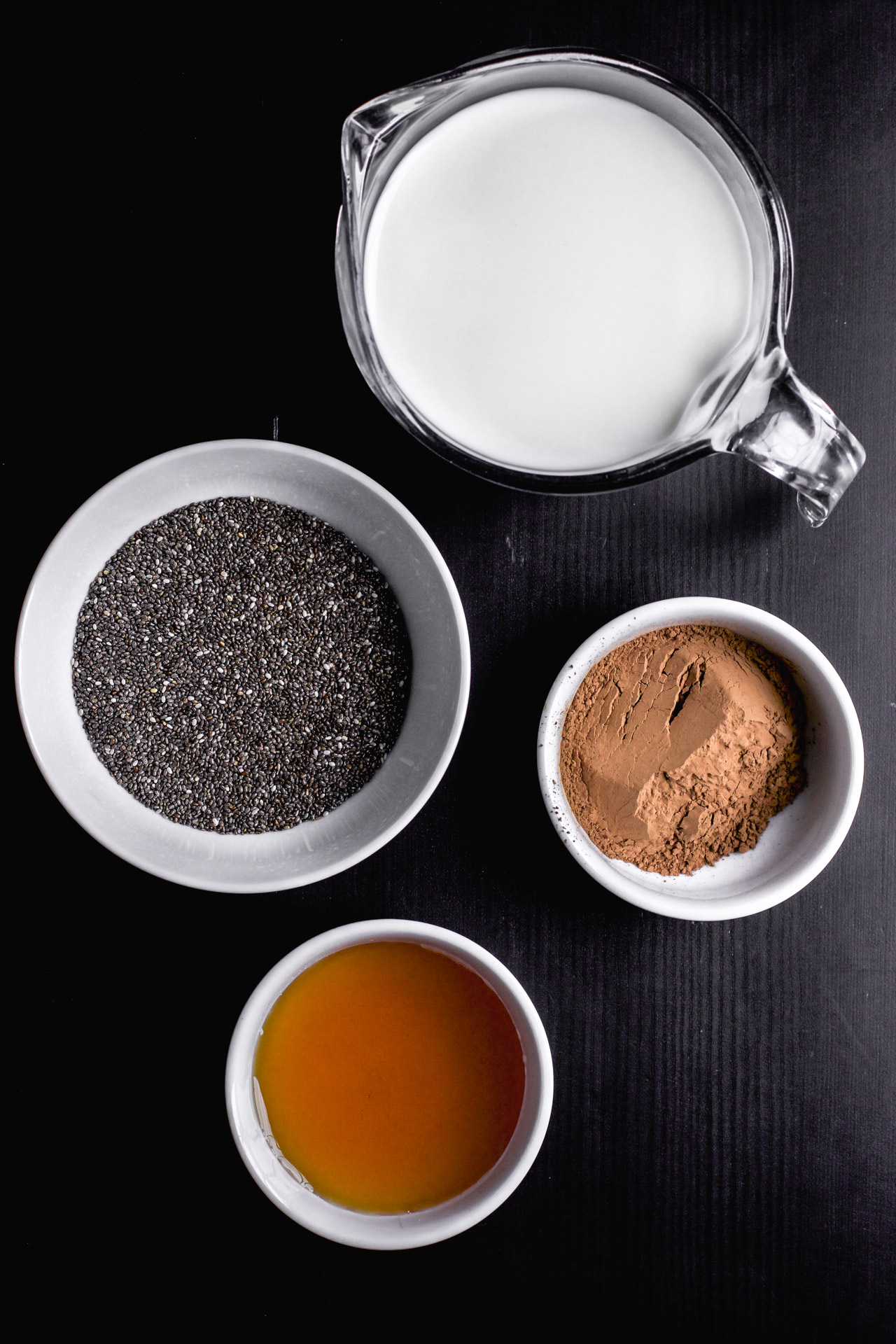 Übersicht der Zutaten für diesen einfachen Chia Schokopudding: Kakaopulver, Milch, Chiasamen und Ahornsirup